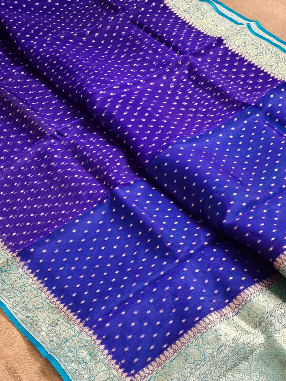 Royal purple and blue patterned fabric, likely a saree, featuring small white dot motifs and a decorative border with turquoise and beige details.