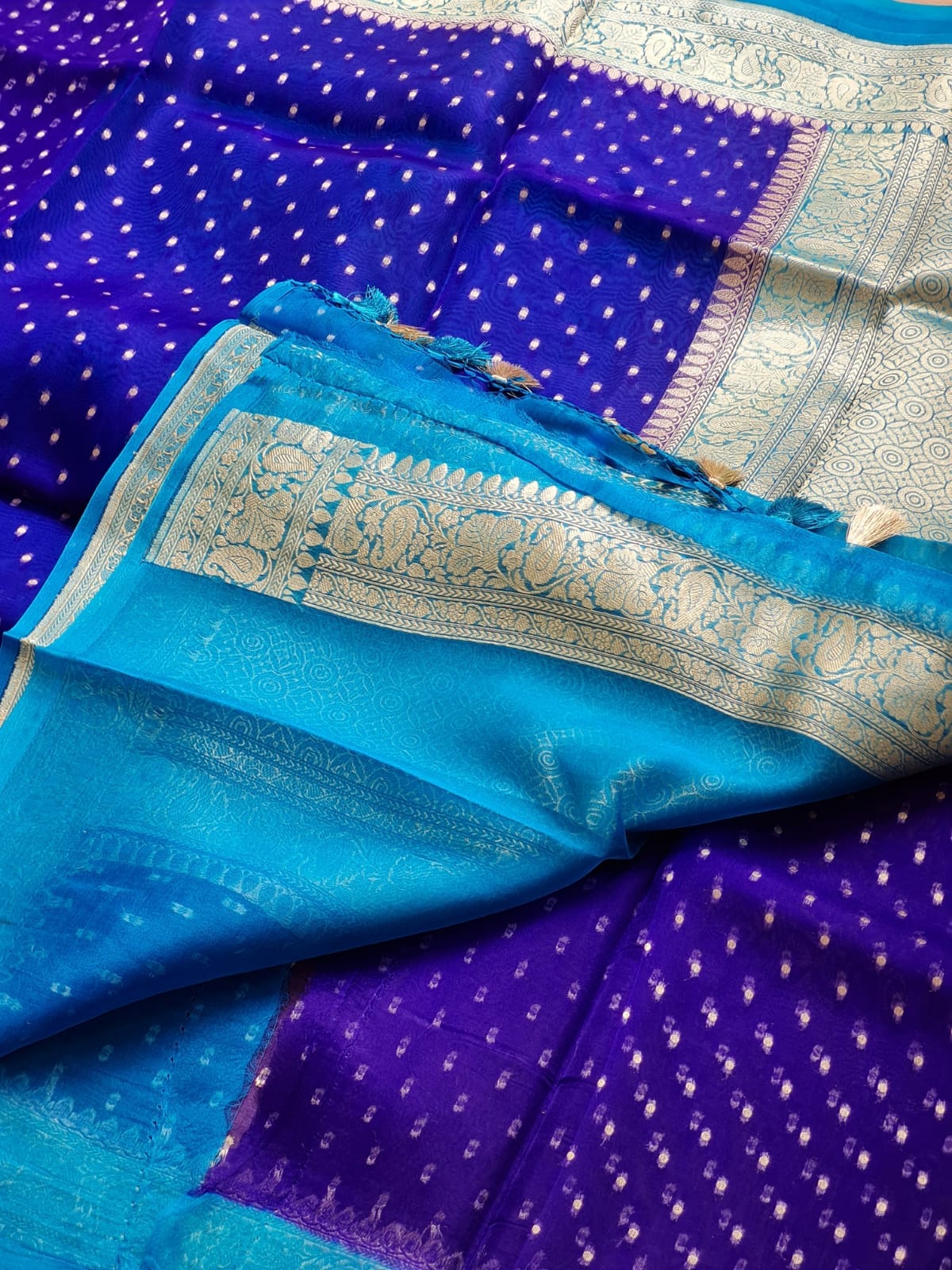 folded silk saree fabric showing a rich royal blue body, a contrasting deep purple border with white dot motifs, and an ornate gold zari brocade.