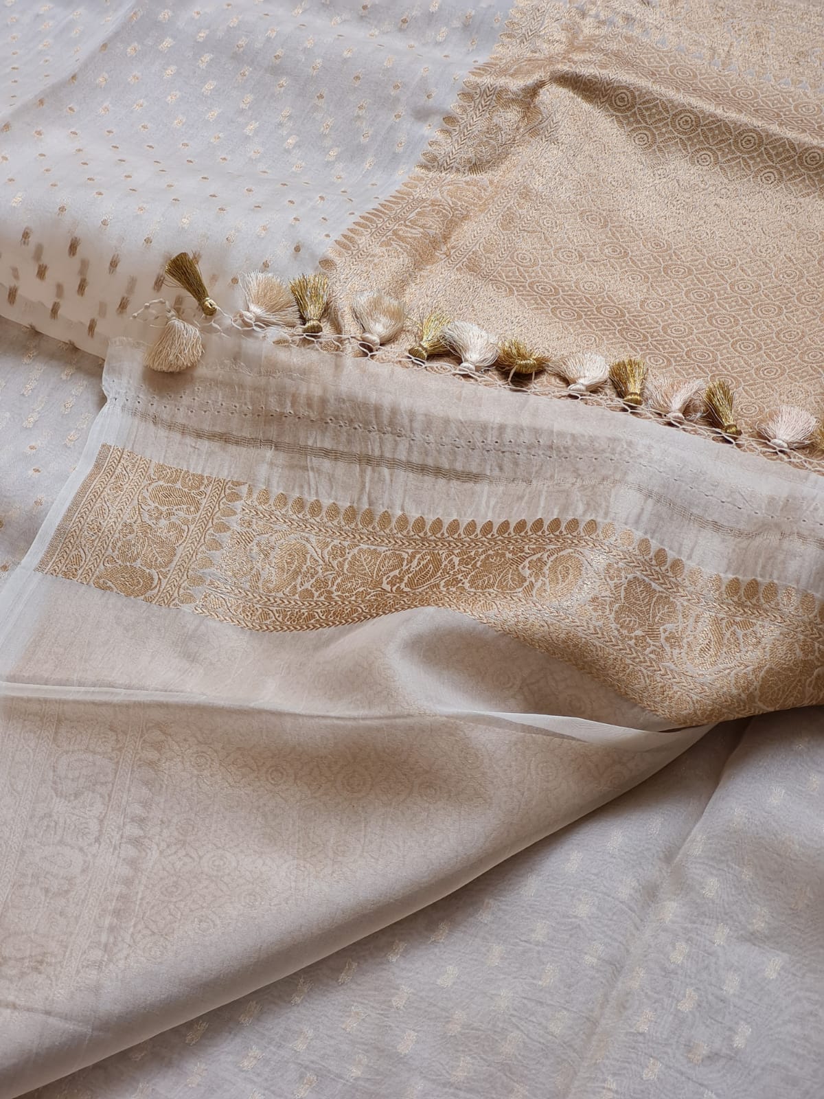 close-up of a beige and off-white fabric set with intricate embroidery, a decorative border, and small tassel details.