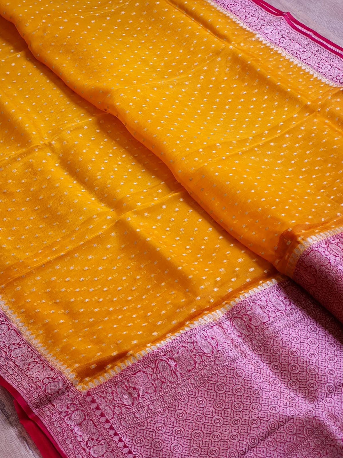 A close-up of a yellow and pink Banarasi silk saree, showing the yellow body with white zari motifs and the pink border with intricate woven patterns.