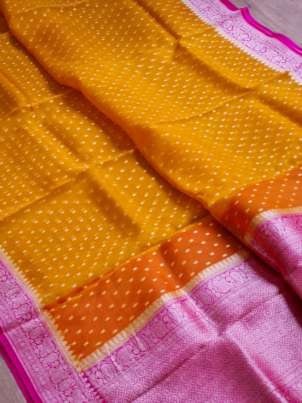 A yellow and orange saree with white dotted patterns, featuring a pink and orange border with a metallic pink zari brocade pallu.