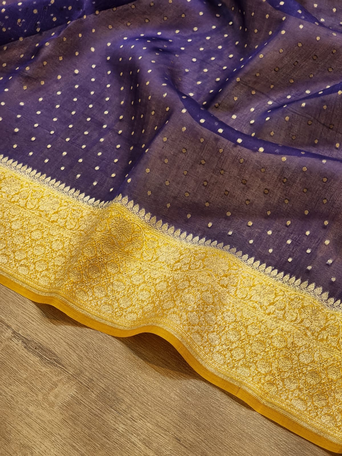 Purple fabric with small metallic gold dots and a wide yellow-gold ornate border, laid over a wood surface.