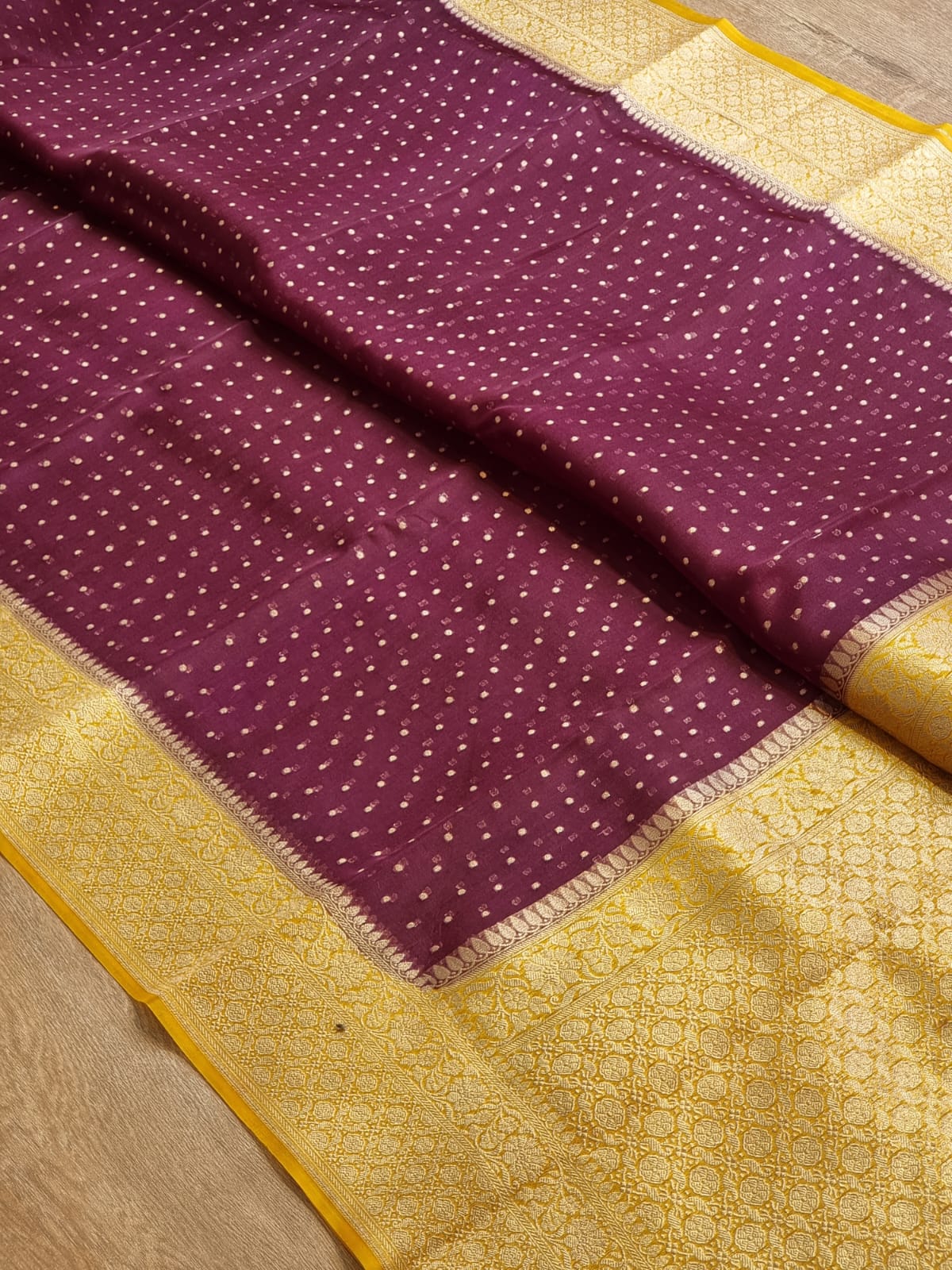 Vine and gold fabric, likely a silk saree, featuring a deep purple body with small gold motifs and a wide gold border with intricate woven patterns.
