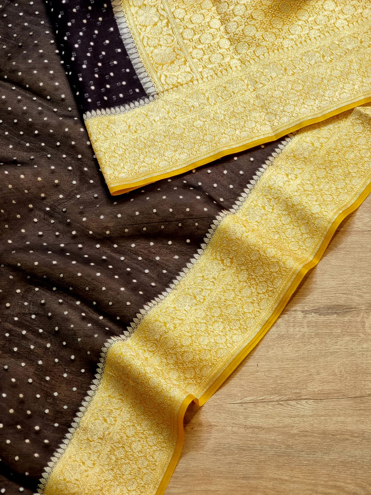 Mustard border and black body patterned fabric with a wide yellow-gold ornate border, laid diagonally on a light wood surface.