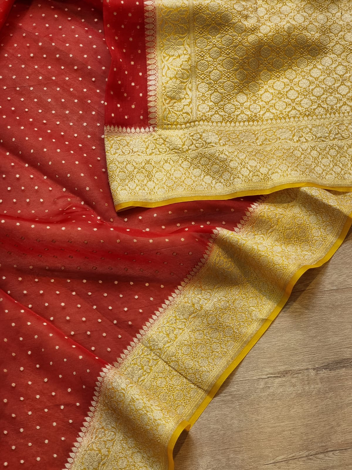 Red and gold Banarasi silk saree, showing the red body with small white dots, a wide gold zari border, and a matching gold pallu draped on a wooden surface.