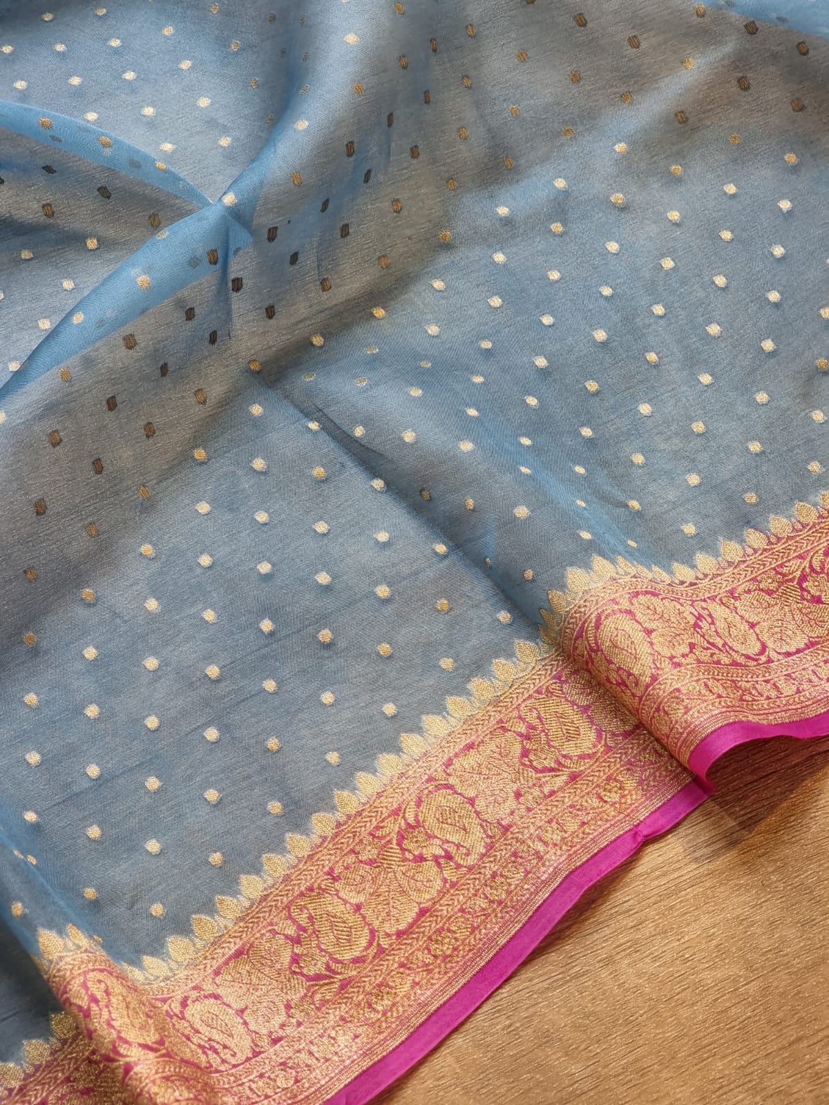 Light blue sheer fabric with small metallic gold dots and a wide pink and gold patterned border, laid on a wooden surface.